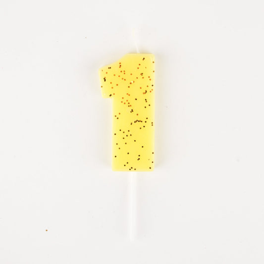 Una candela gialla numero 1 anno con glitter per una torta frizzante