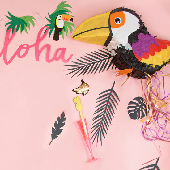Tropical birthday decoration with toucan pinata and tropical leaves.